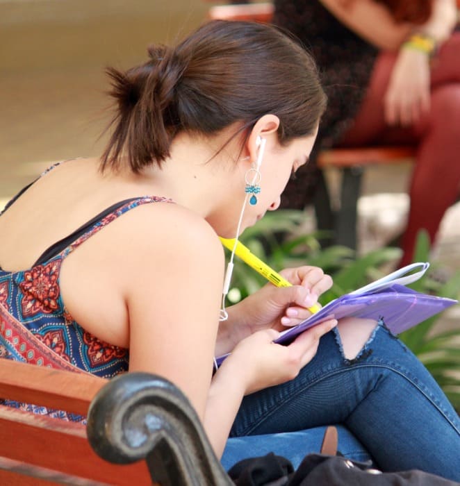 Estudiante repasa su cuaderno al interior de campus universitario.