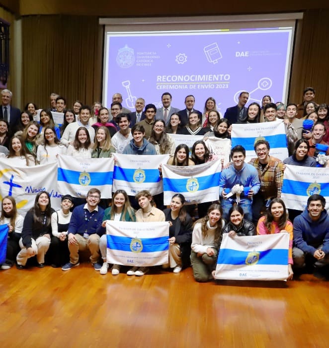 Grupo de estudiantes de la UC sostienen banderas de la universidad y posan junto a autoridades en ceremonia de envío en Casa Central.