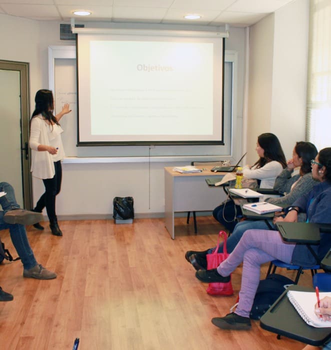 Profesora dicta charla frente a estudiantes de la UC al interior de sala en campus.