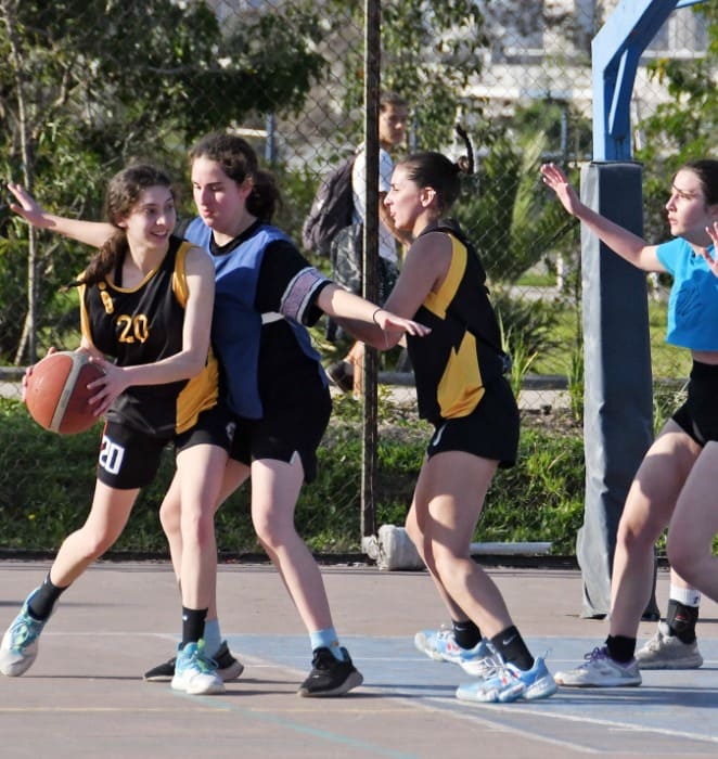 Grupa de alumnas participa en partido de básquetbol al interior de campus universitario.