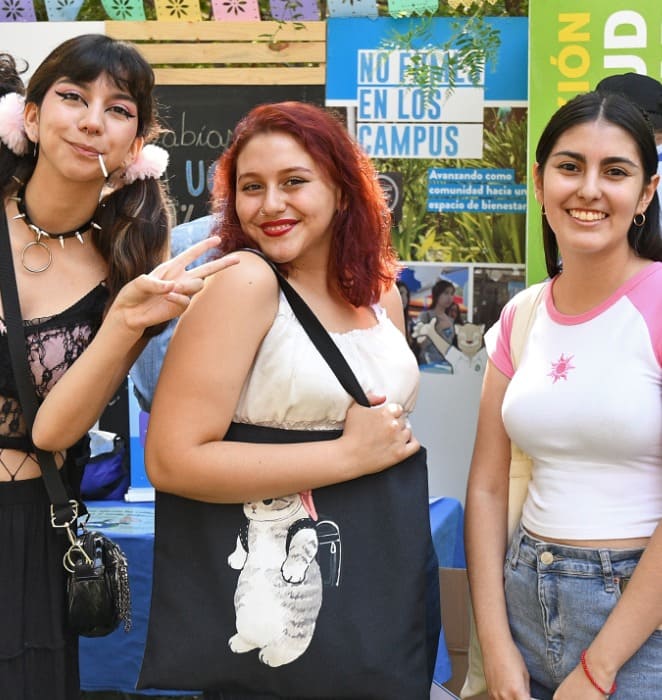 Tes alumnas de la PUC sonríen a la cámara mientras participan de actividad al aire libre al interior del campus San Joaquín.