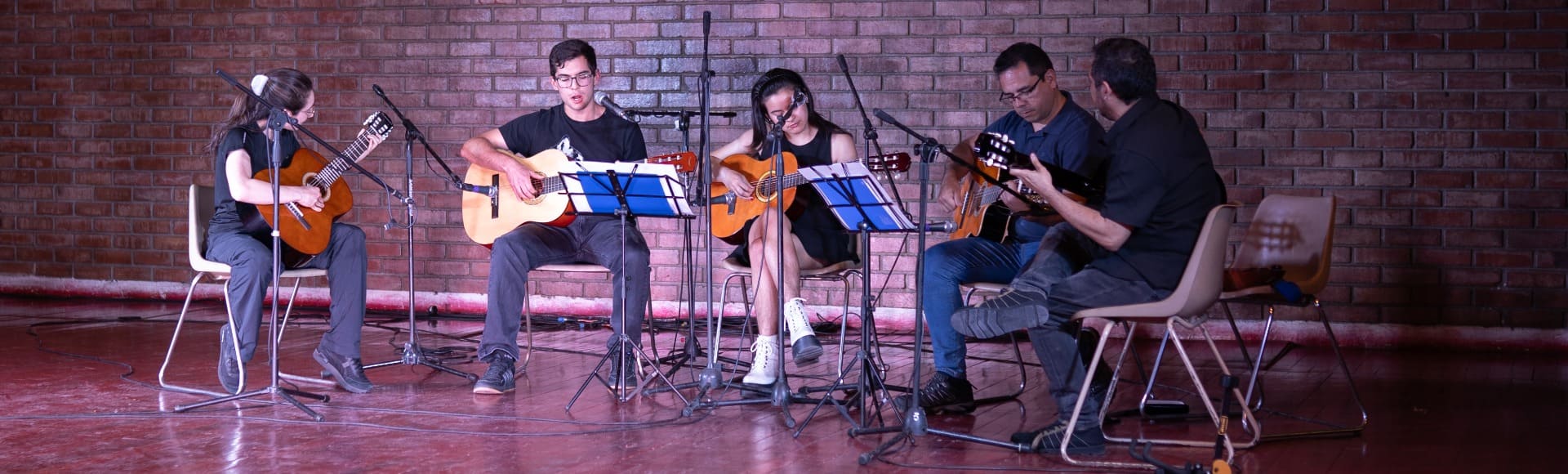 Estudiantes se  presentan tocando la guitarra en medio de ceremonia de gala de los talleres artísticos culturales impartidos en la PUC.