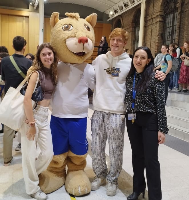 Tres estudiantes internacionales, posando junto a la mascota UC, en una ceremonia realizada en Casa Central UC.