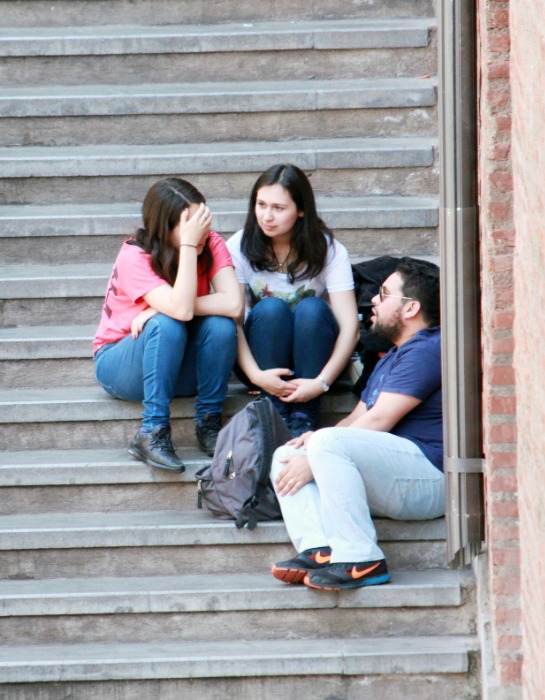 Tres estudiantes conversan sentados en una escalera al interior del campus Casa Central de la PUC.