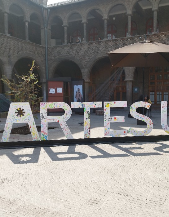 Imagen muestra logo de Artes UC en el patio central del Campus Oriente.