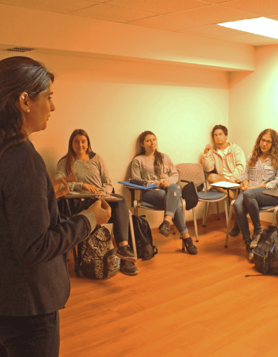 Estudiantes atentos en una sala observando y escuchando a una persona exponer