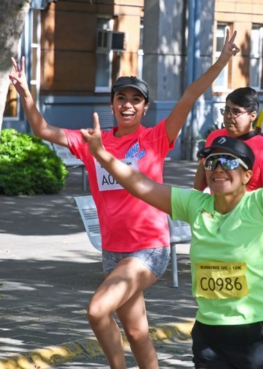 Destacada Running UC 2025. Mujer participando de la corrida y saludando a la cámara.