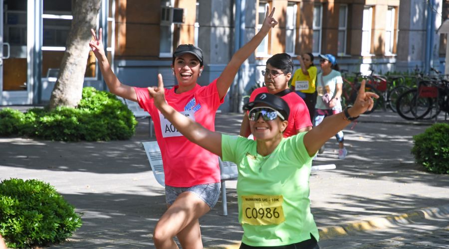Running UC 2025. Mujer participando de la corrida y saludando a la cámara.